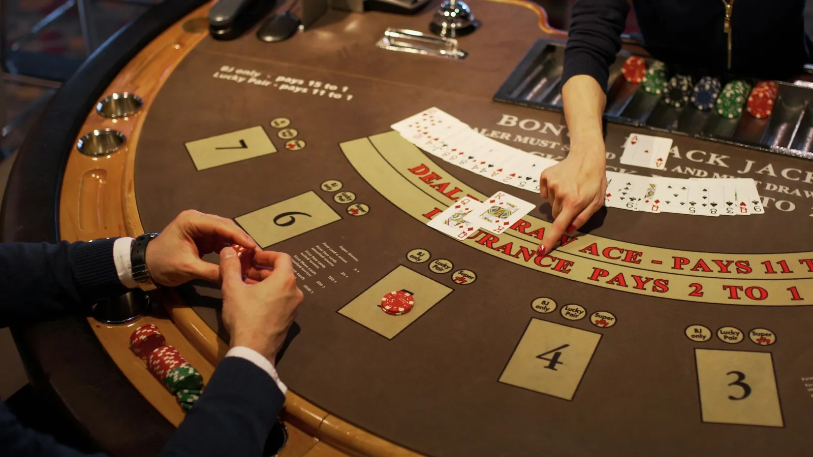 Player and dealer hands over a live blackjack table mid-round, chips and cards on the felt