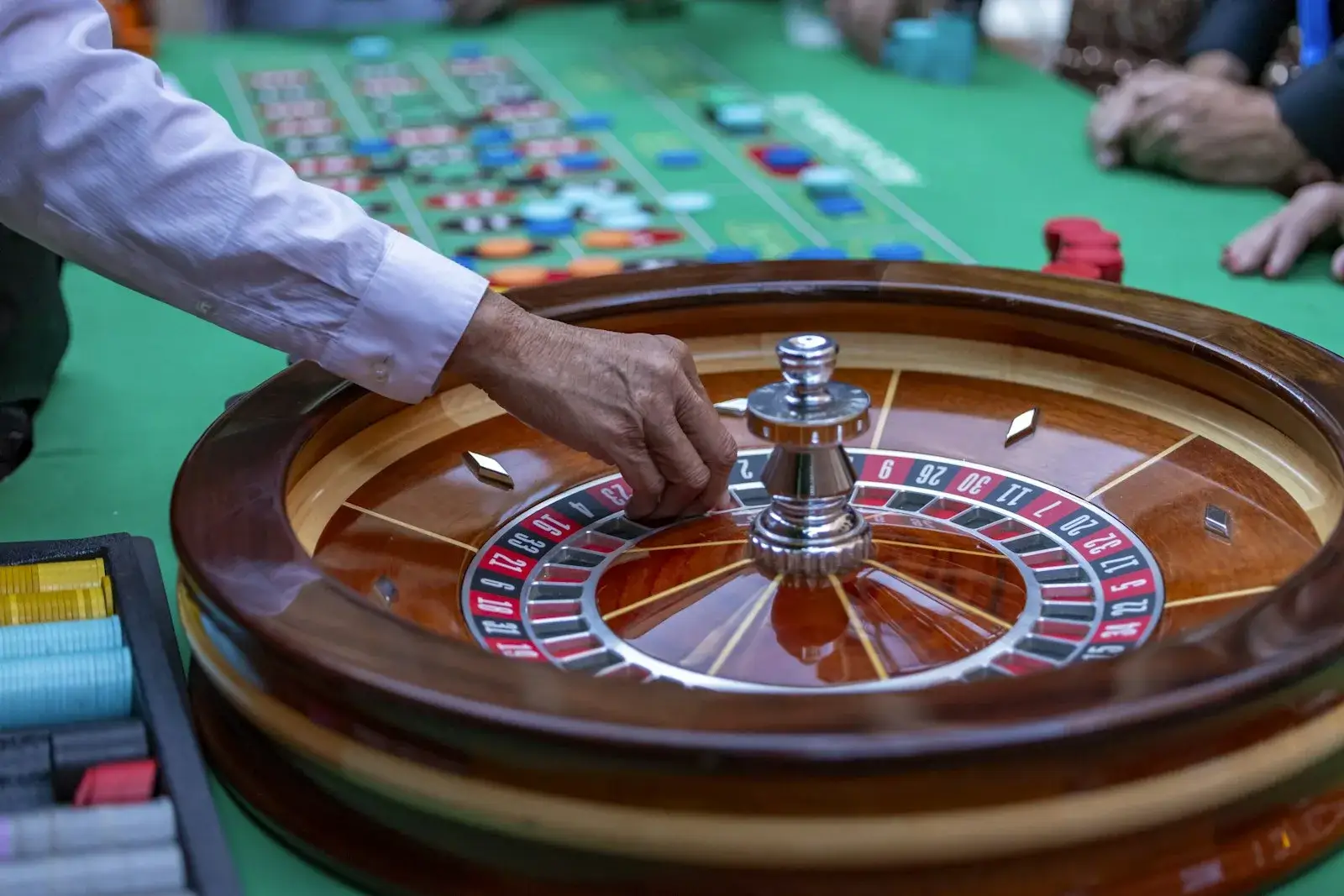 Dealer hand spinning a wooden roulette wheel next to a marked betting layout with chips